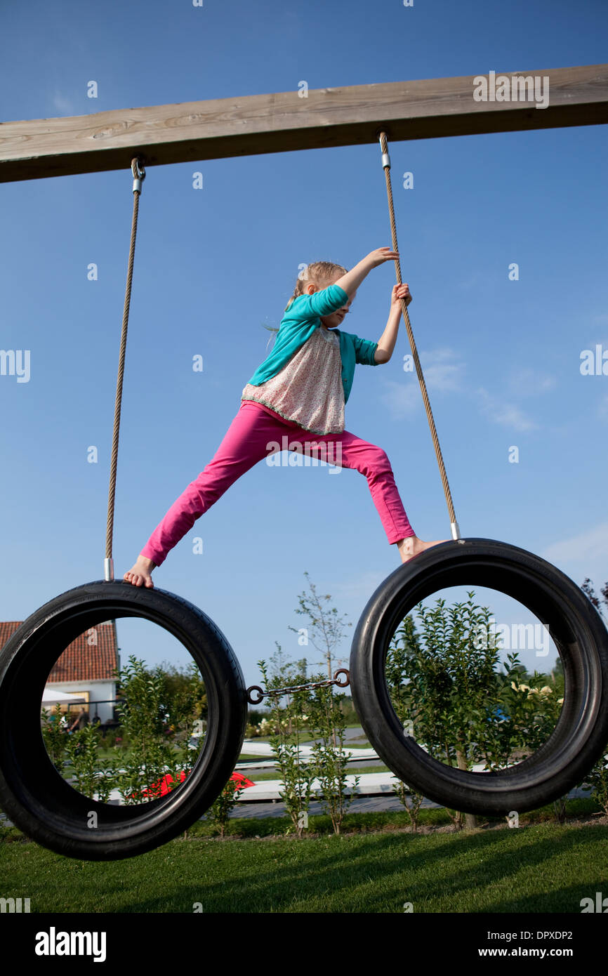 Ragazza salendo attraverso due pneumatici di rotazione in corrispondenza di un parco giochi per bambini Foto Stock