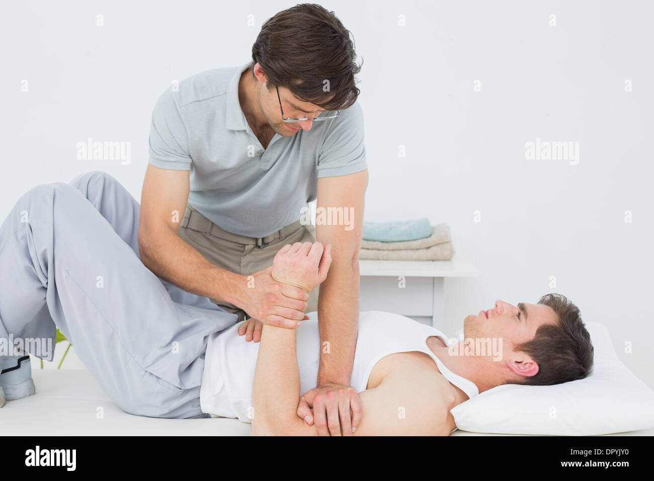 Fisioterapista maschio esaminando un giovane mans mano Foto Stock