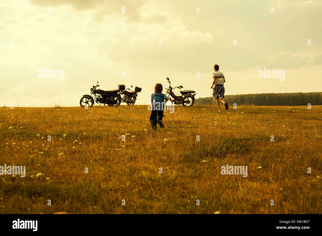Ragazzi in esecuzione per i motocicli nel paesaggio rurale Foto Stock