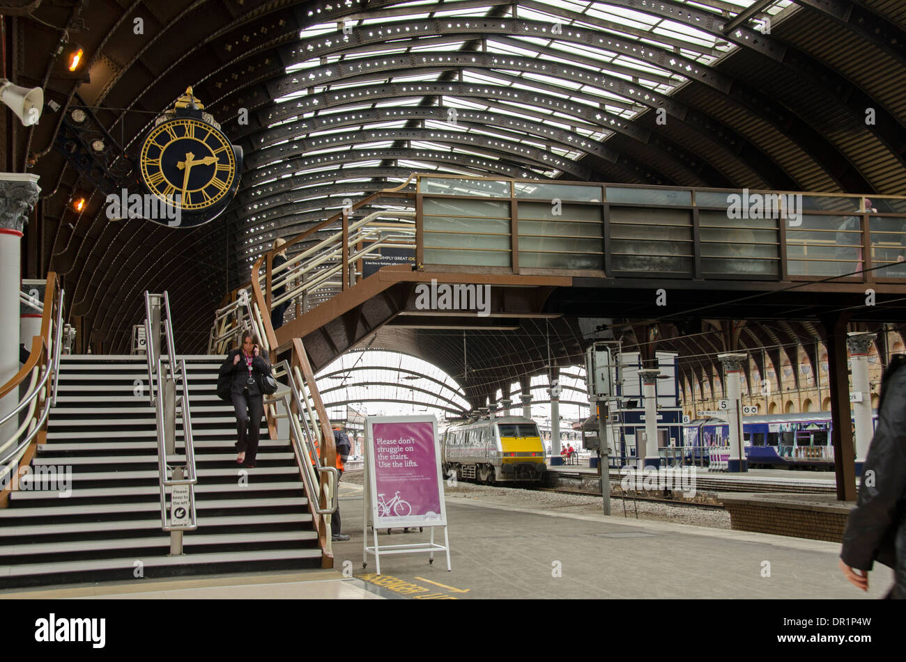 Interno del trainshed con ferro e il tetto in vetro fisso, treni & donna a piedi dalla piattaforma orologio - La stazione ferroviaria di York, North Yorkshire, Inghilterra, Regno Unito Foto Stock