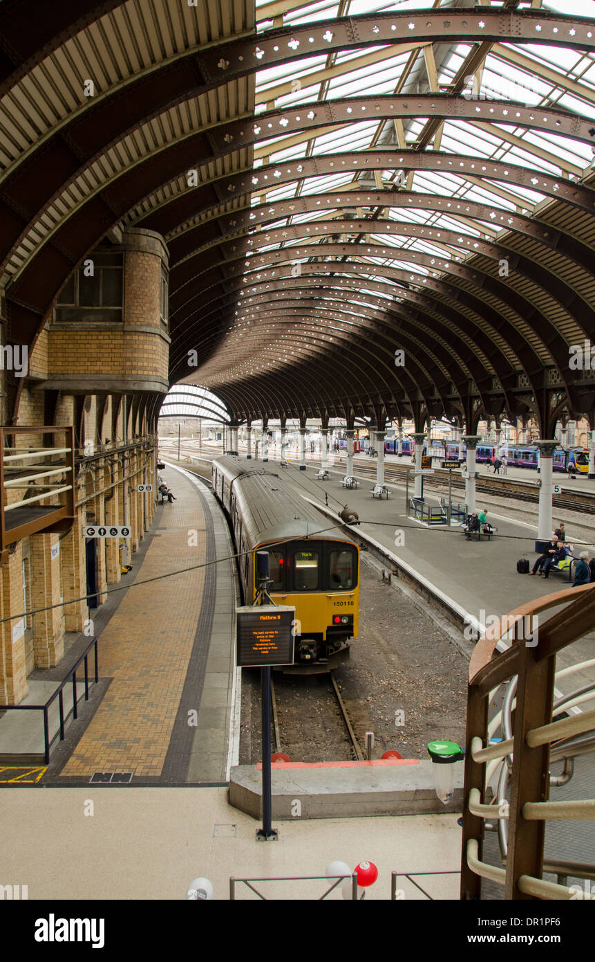 Vista interna di trainshed con ferro e il tetto in vetro fisso, treni & persone in attesa su platfom - La stazione ferroviaria di York, North Yorkshire, Inghilterra, Regno Unito. Foto Stock