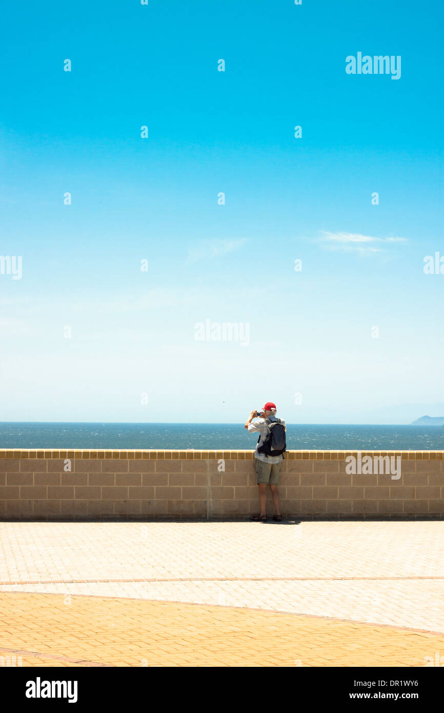 Un uomo prendendo foto di paesaggi marini su blu cielo privo di nuvole Foto Stock