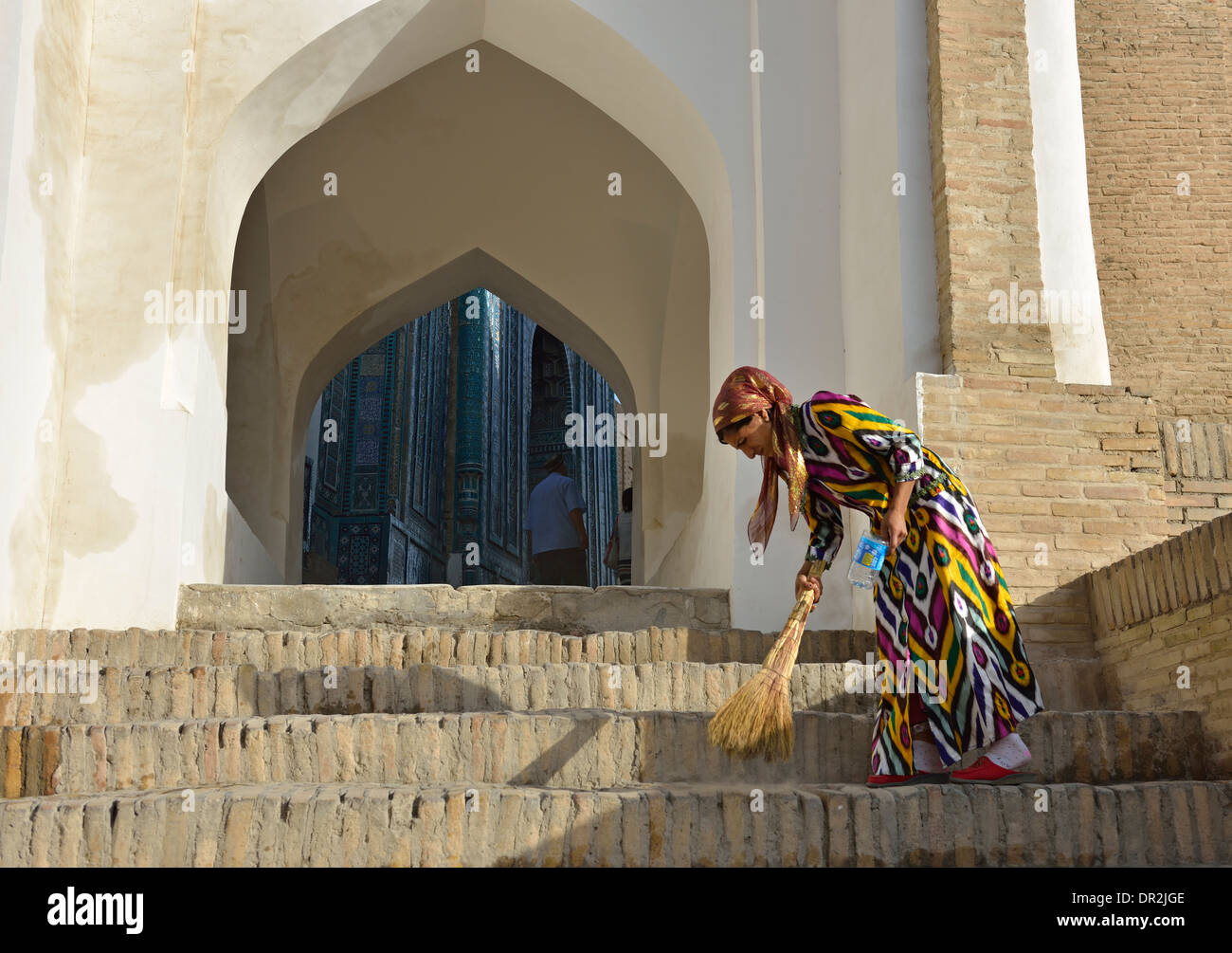 Donna spazzare dall ingresso di Shah-i-Zinda mausoleo complessa, Samarcanda, Uzbekistan Foto Stock