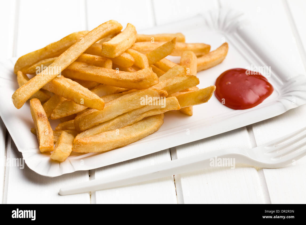 Patate fritte con ketchup sul piatto di carta bianco sul tavolo di legno Foto Stock