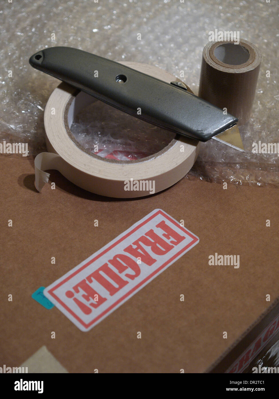 Materiali di imballaggio comprendente una scatola con l'etichetta "Fragile", un mestiere coltello, bubble-wrap e bobine di nastro. Foto Stock