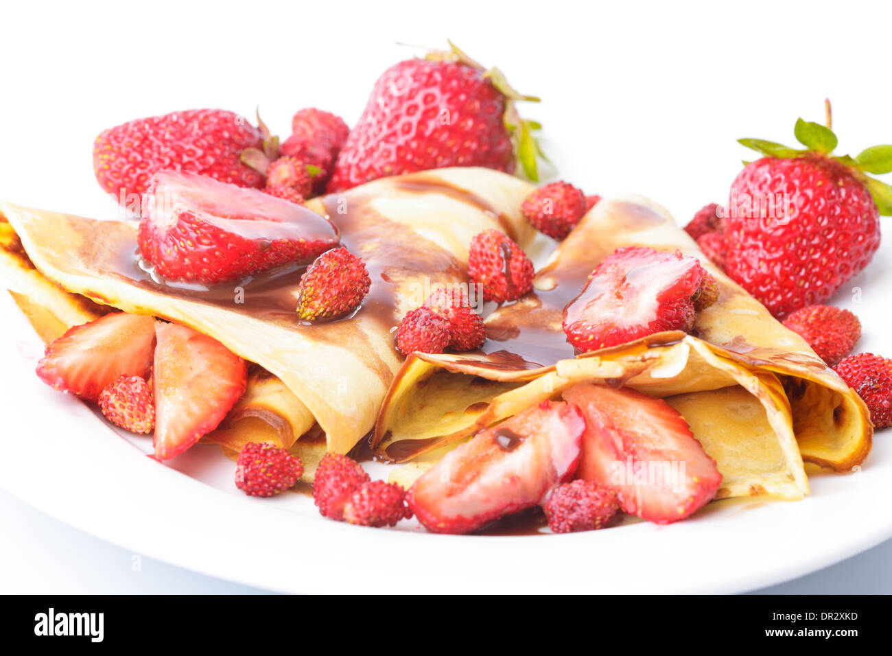 Frittelle con differenti le fragole con lo sciroppo di cioccolato su bianco Foto Stock