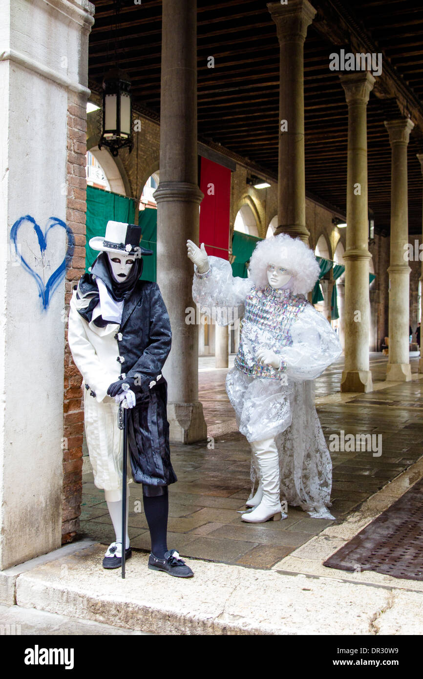 Mascherato e partecipanti in costume di carnevale di Venezia in posa per fotografie con un cuore sulla parete Foto Stock