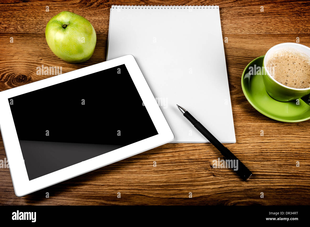 Compressa con una schermata vuota vicino a una penna e tazza verde e Apple Foto Stock