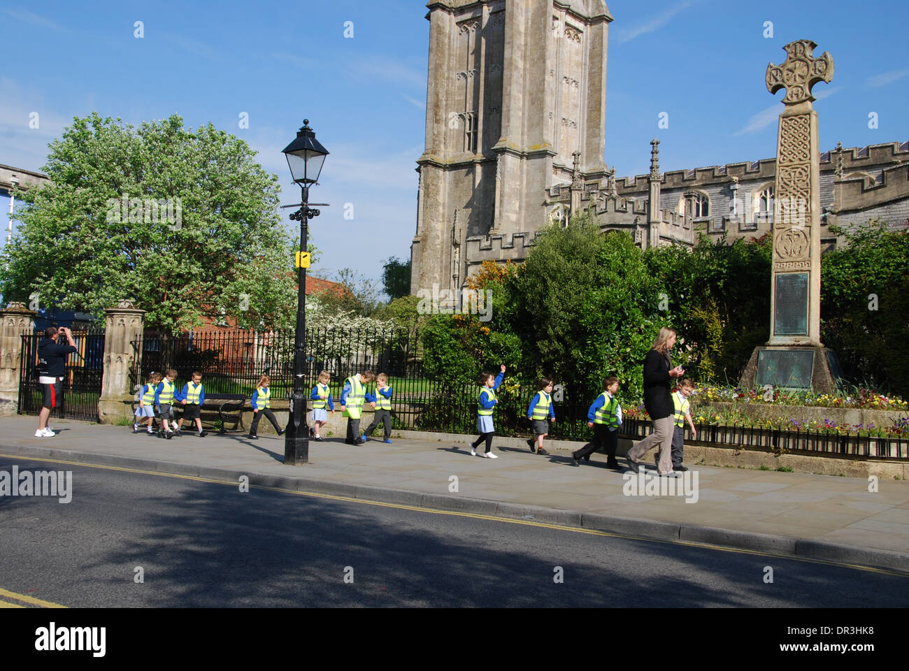 Glastonbury High Street con la scuola classe passando la chiesa di San Giovanni Battista Somerset Inghilterra Foto Stock