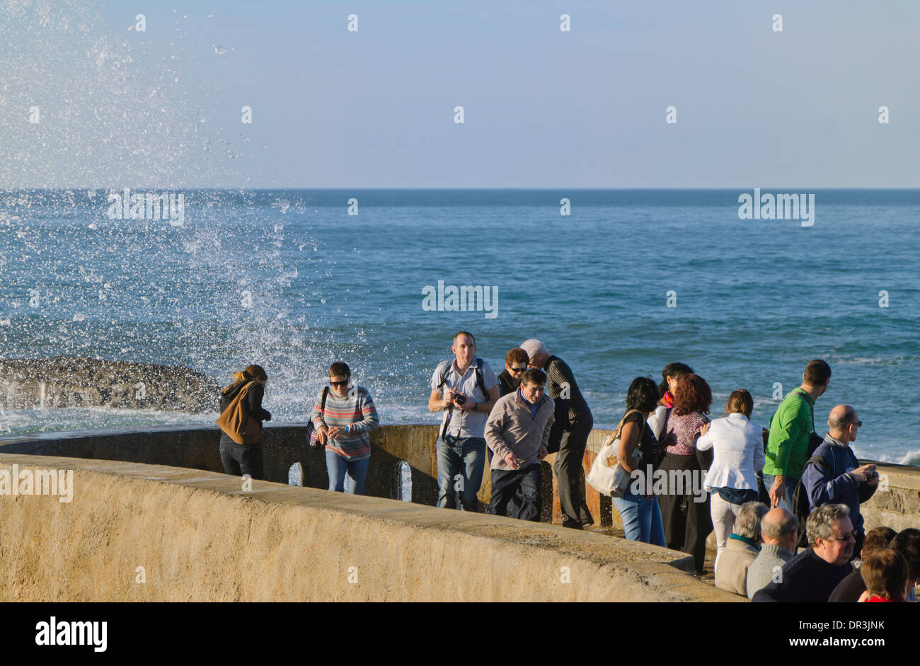 I turisti sono sorpresi da Biarritz alta marea grandi onde che sbattevano il molo del Rocher de la Vierge. Biarritz, Francia. Foto Stock