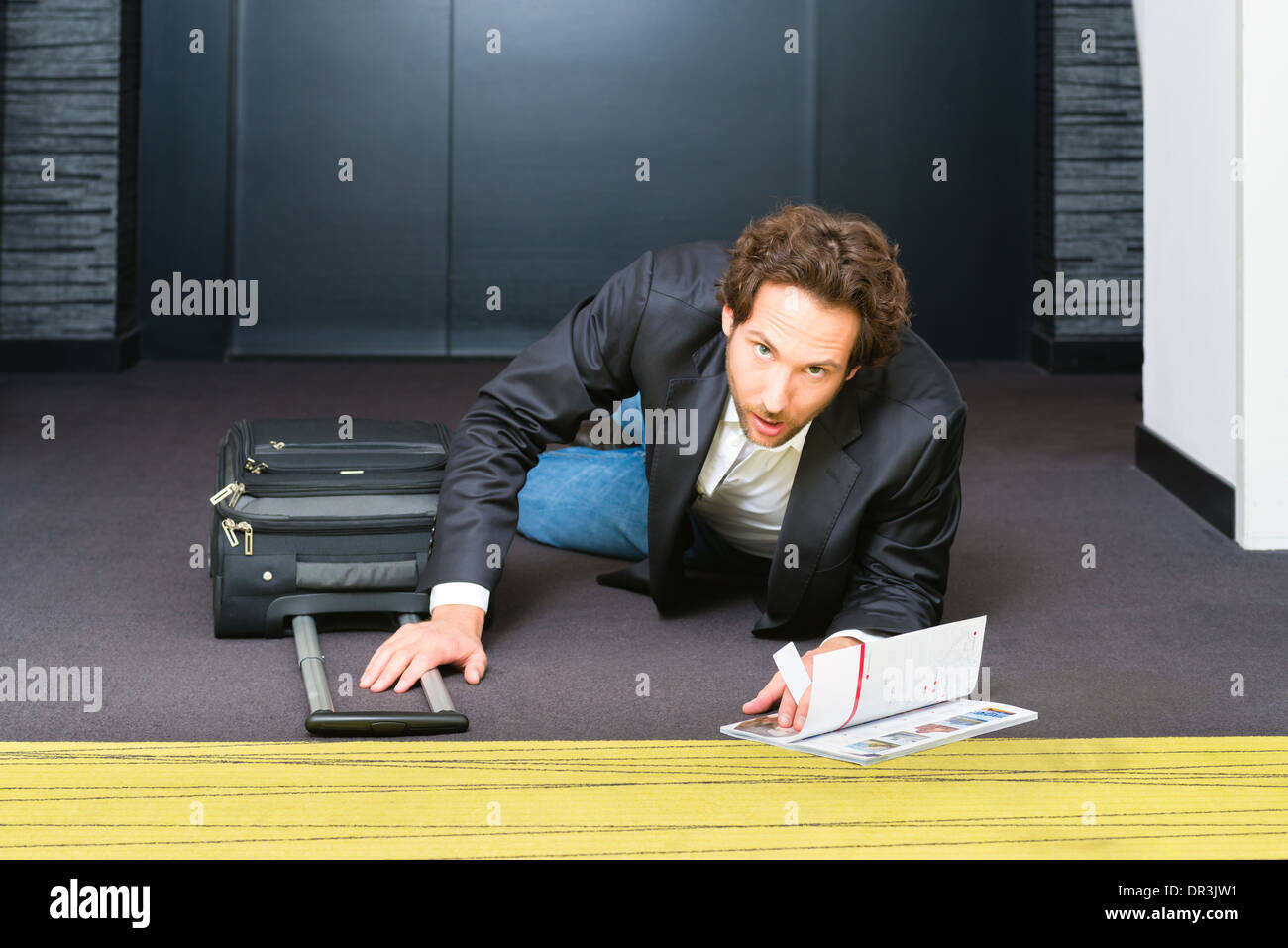 Giovane uomo nel corridoio dell'albergo è incappato in fretta lungo i bagagli e la valigia e ora giace sul pavimento Foto Stock