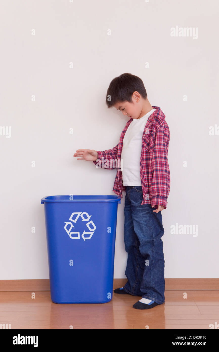 Ragazzo di mettere la bottiglia di plastica nel contenitore di riciclaggio Foto Stock