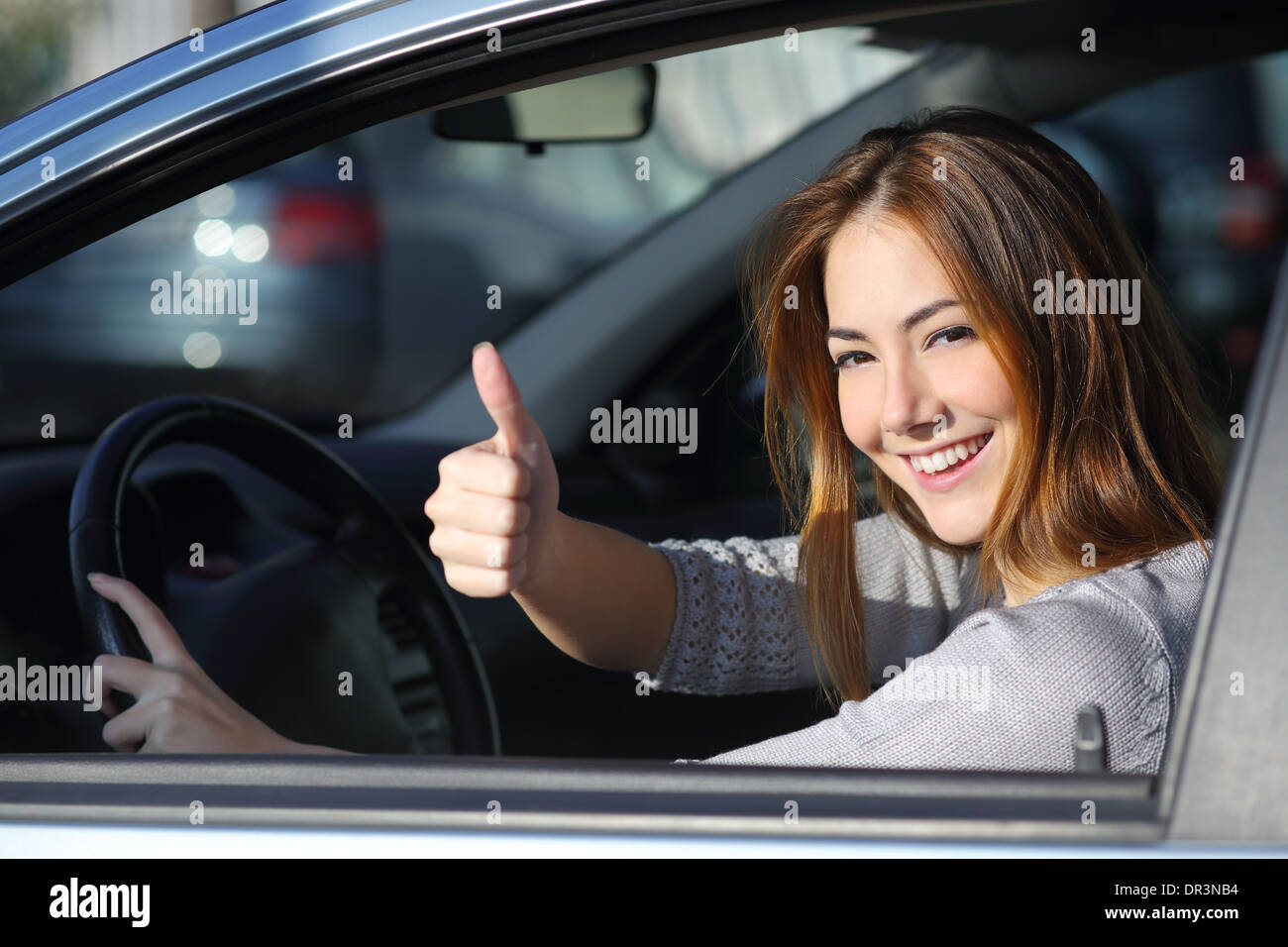 Donna felice all'interno di un guida auto in strada e gesticolando pollice in alto Foto Stock