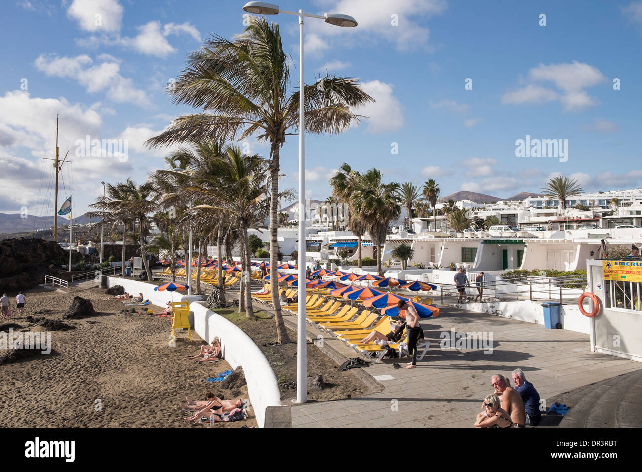 Bianco tipico Holiday appartamenti sul lungomare fiancheggiata con lettini che si affaccia su Playa Chica spiaggia di Puerto del Carmen Lanzarote Foto Stock