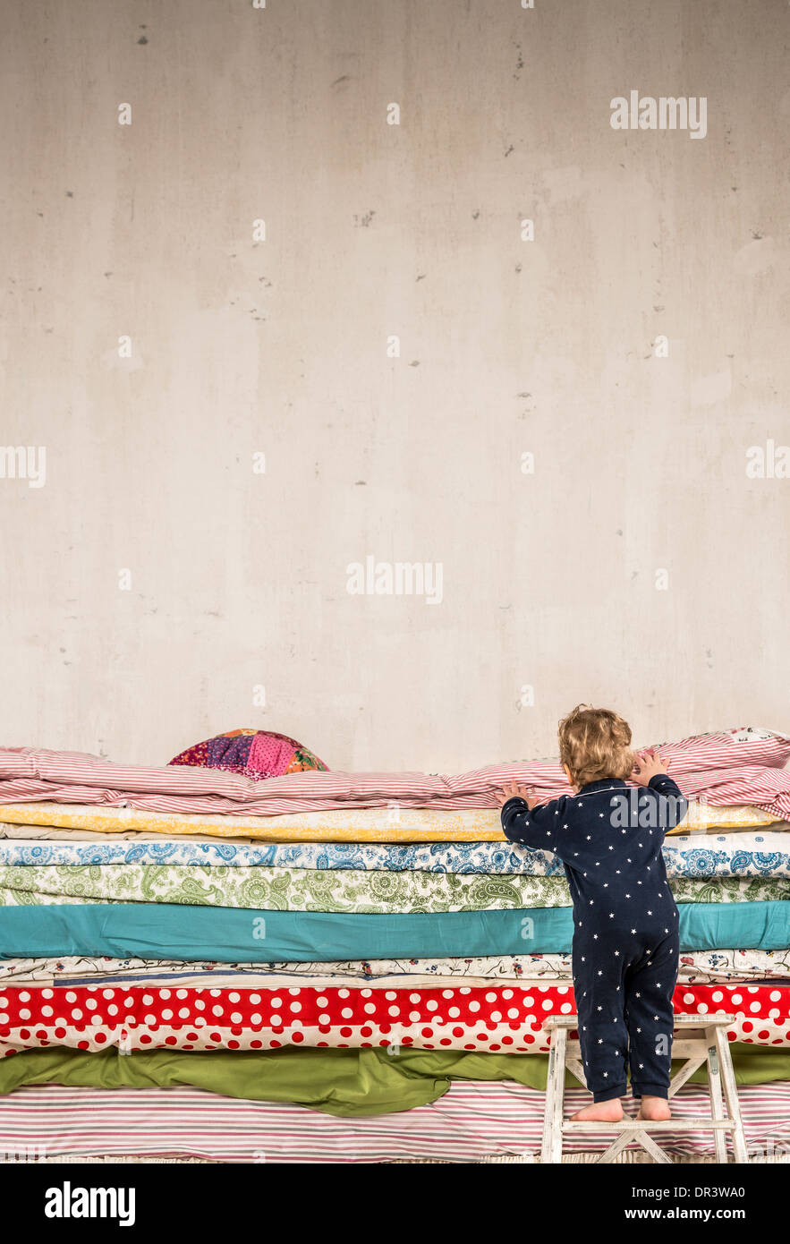 Il bambino si arrampica sul letto con un sacco di trapunte - La principessa sul pisello. Foto Stock