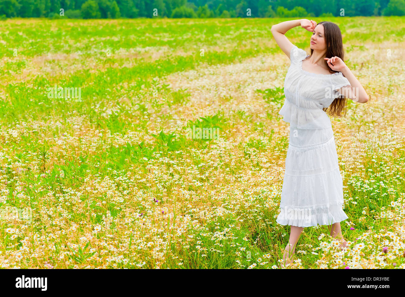 Bruna giovane donna che cammina in un campo con margherite Foto Stock