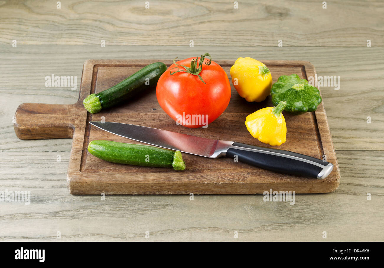 Foto orizzontale di crudo fresco baby squash, il pomodoro e il coltello sul noce nero con bordo legno invecchiato sotto Foto Stock