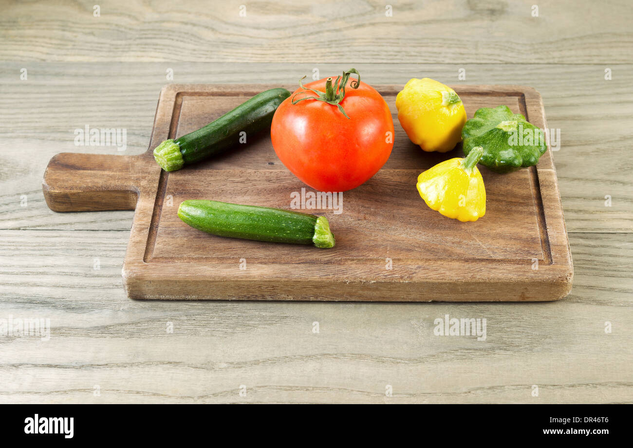 Foto orizzontale di crudo fresco baby squash e pomodoro sul noce nero con bordo legno invecchiato sotto Foto Stock