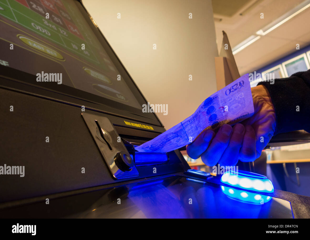 Uomo di mettere venti pound nota in fixed odds macchina da gioco di coralli betting shop. Regno Unito Foto Stock