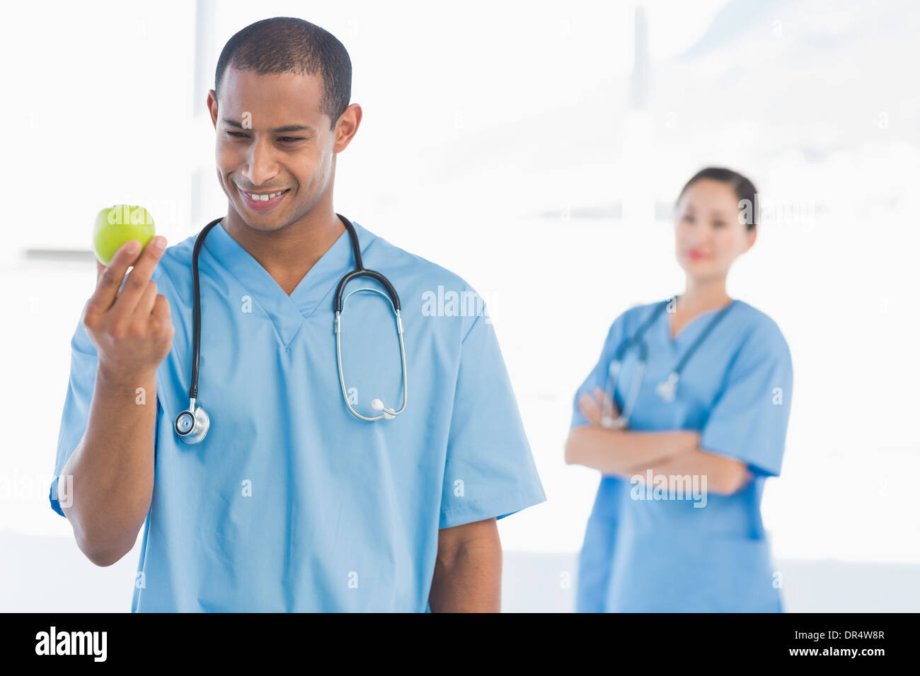Chirurgo maschio tenendo un Apple con il collega dietro Foto Stock