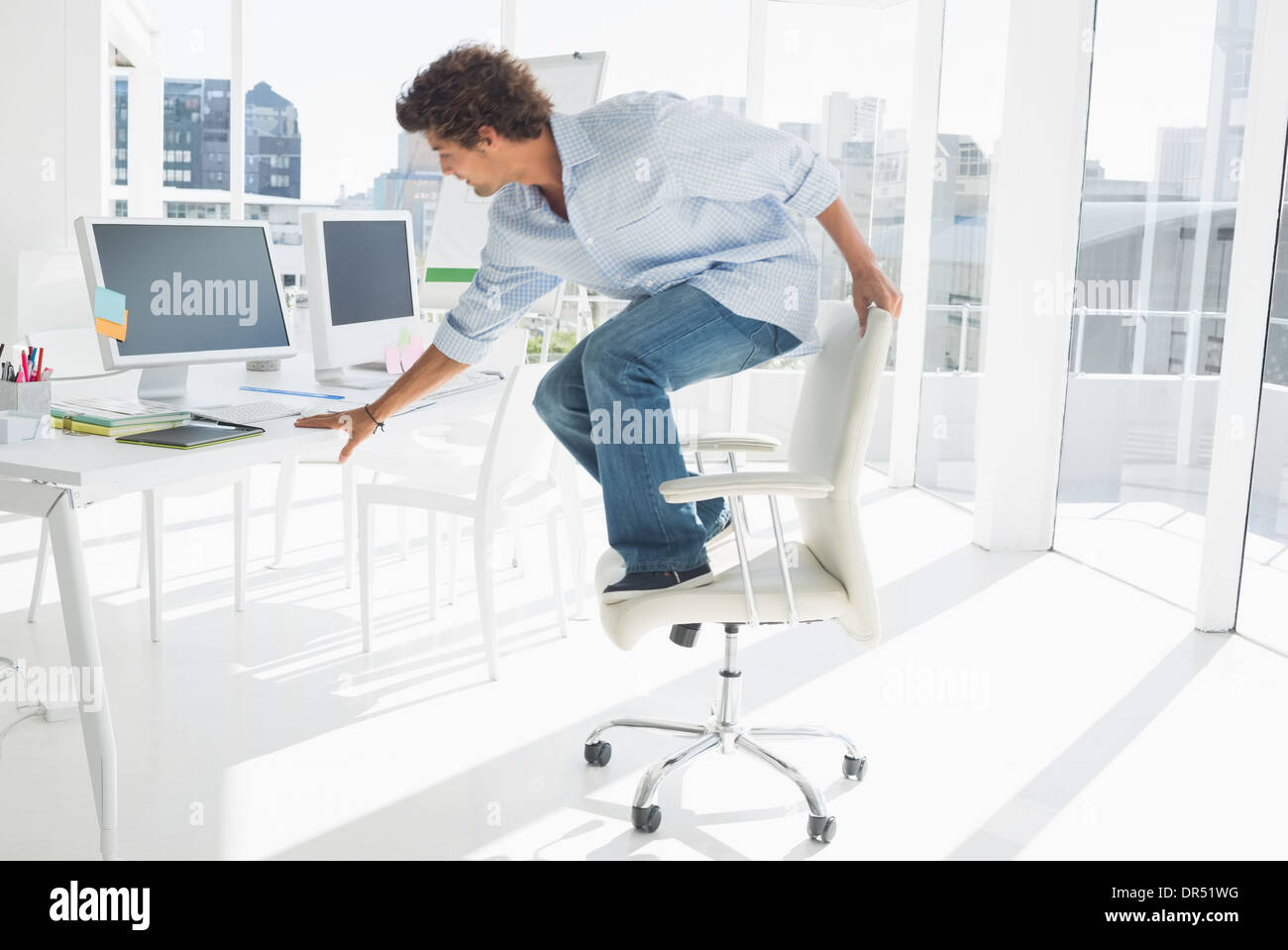 Giovane uomo in piedi sulla sedia in ufficio luminoso Foto Stock