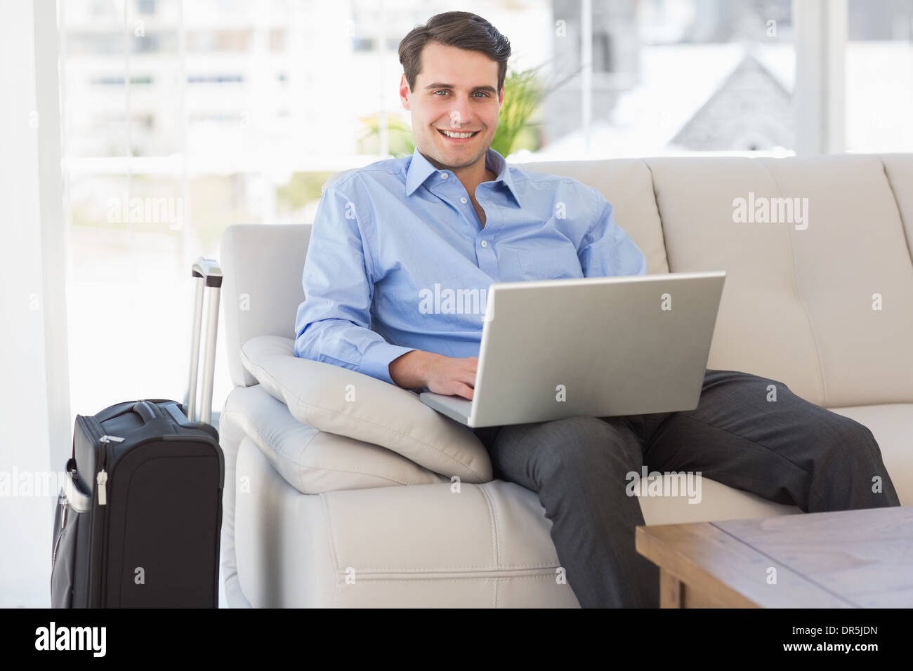 Viaggia per lavoro utilizzando laptop seduto sul divano sorridente in telecamera Foto Stock