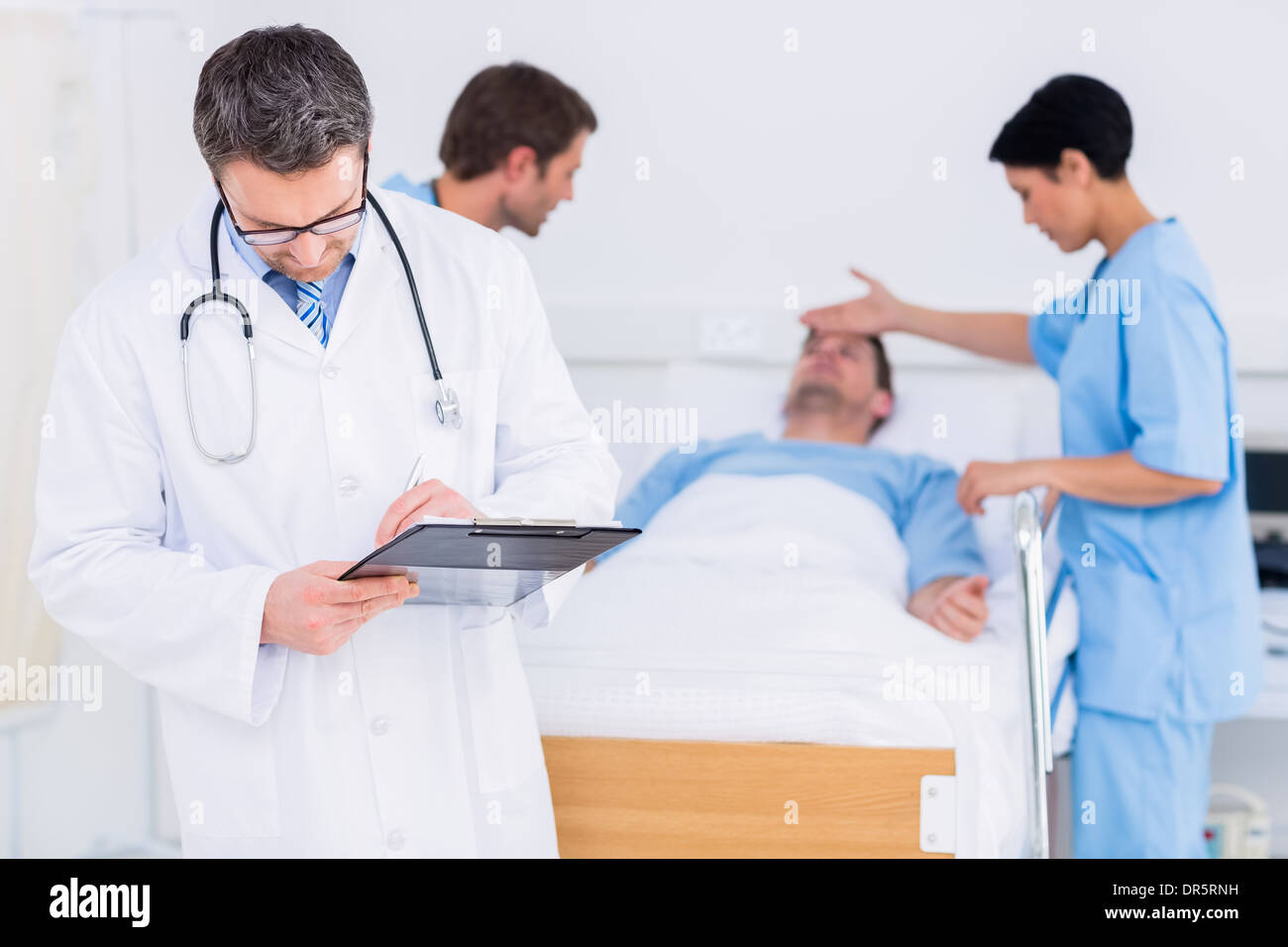 Medico scrivere rapporti con il paziente ed il chirurgo in background Foto Stock