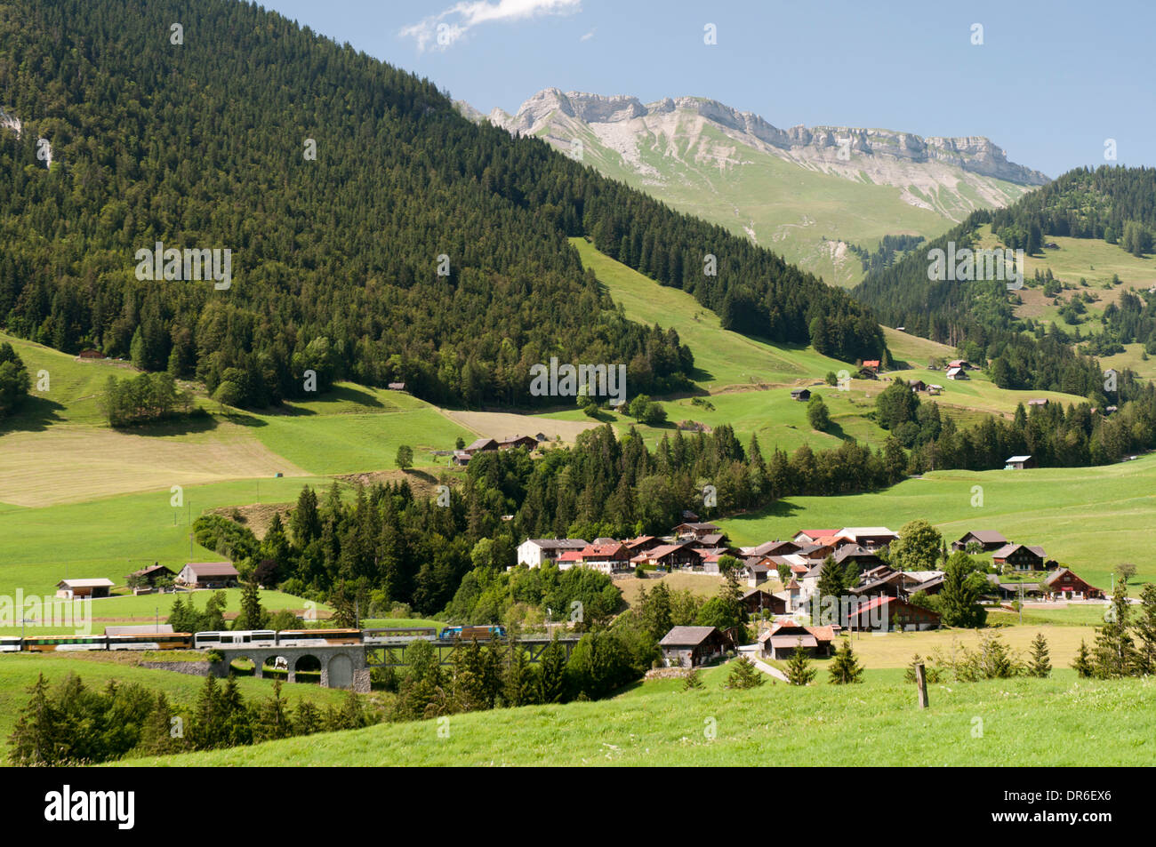 Vista del villaggio di Flendruz e un treno attraversando un ponte nella valle Saane nelle Alpi Svizzere Foto Stock