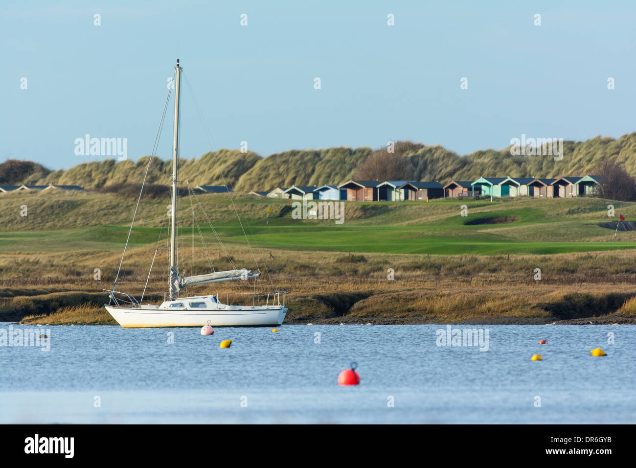 Cabine sulla spiaggia, Brancaster sul campo da Golf, con yacht nel canale di marea. Foto Stock