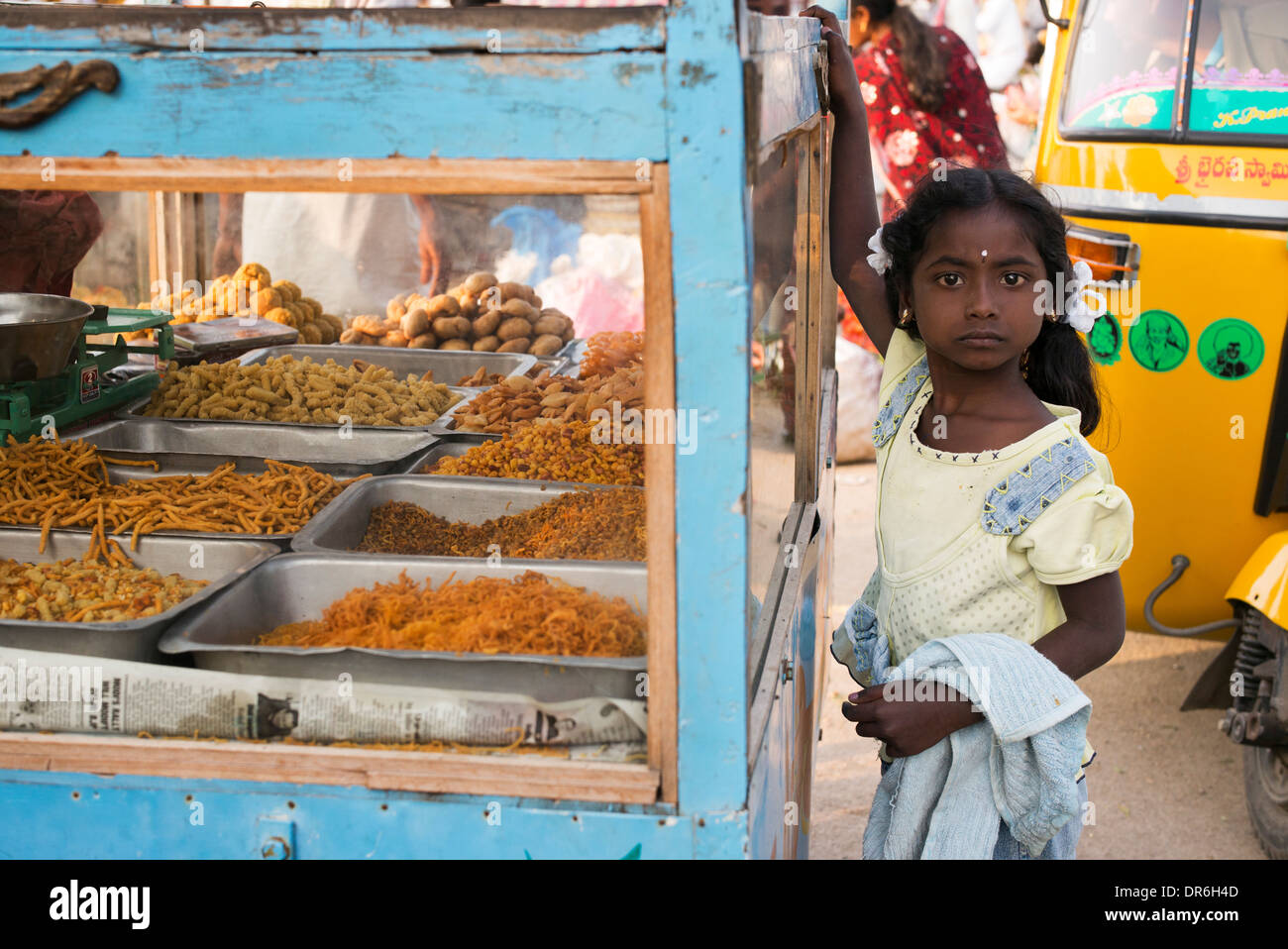 Giovane ragazza indiana in piedi accanto a un dolce e snack fritti stallo a un mercato indiano. Puttaparthi, Andhra Pradesh, India Foto Stock