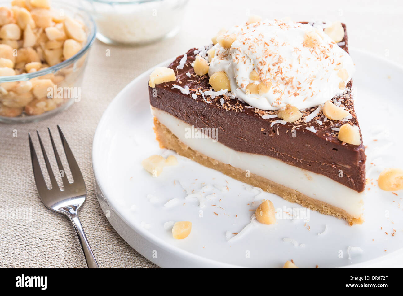 Haupia decadente e crema al cioccolato torta guarnita con radere noce di cocco, noci di macadamia e scaglie di cioccolato con panna montata Foto Stock