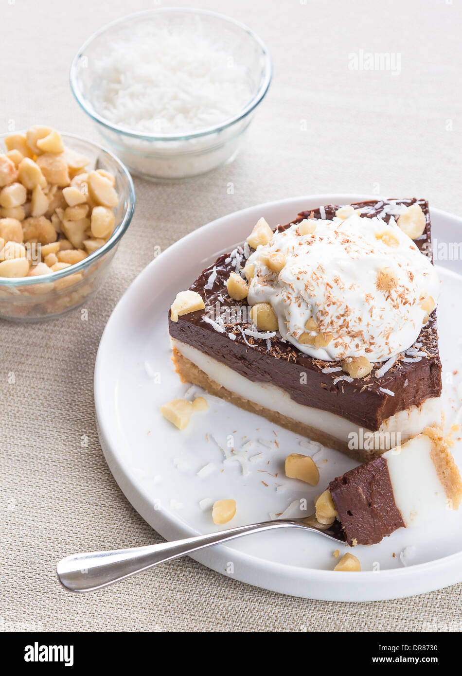 Haupia decadente e crema al cioccolato torta guarnita con radere noce di cocco, noci di macadamia e scaglie di cioccolato con panna montata Foto Stock