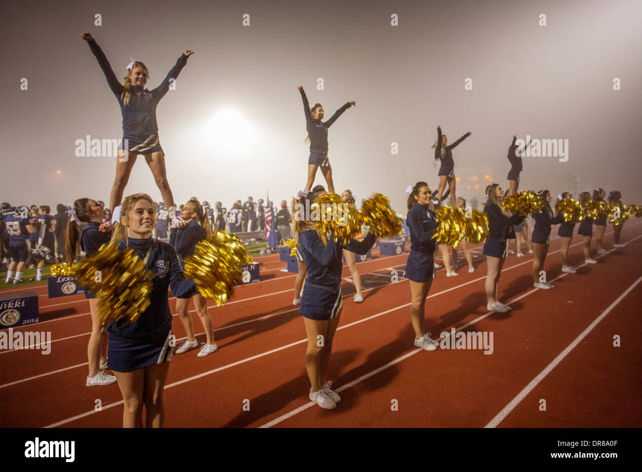 Cheerleaders divertire gli spettatori in una scuola di notte del gioco del calcio in San Juan Capistrano, CA, tenere le iniziali del nome della scuola. Nota 'volantini" sulle spalle di altre cheerleader. Foto Stock