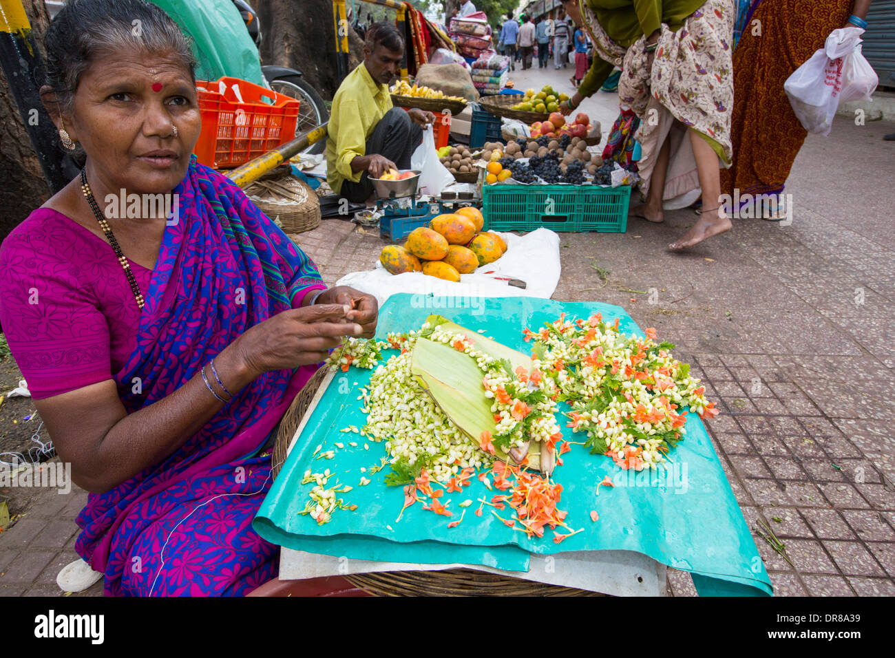 Una donna che fa floral decorazioni capelli ad una strada del mercato di Mysore, India. Foto Stock