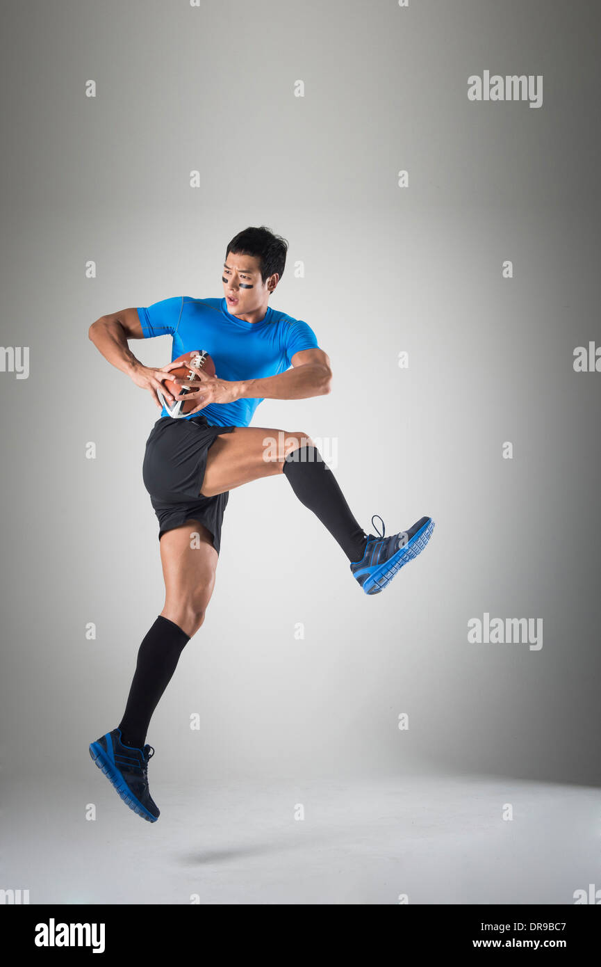 Montare un Uomo in camicia blu jumping con palla da rugby Foto Stock