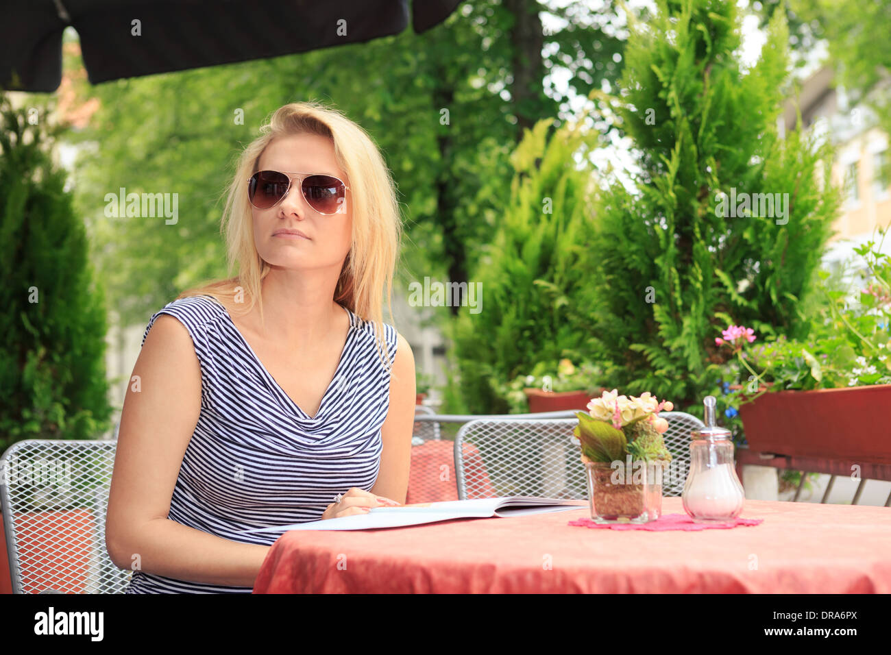 Una giovane donna seduta a un cafè sul marciapiede Foto Stock