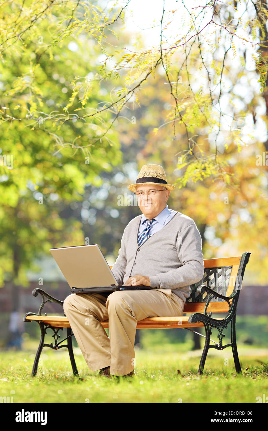 Senior gentleman lavorando su laptop seduto sulla panca di legno in posizione di parcheggio Foto Stock