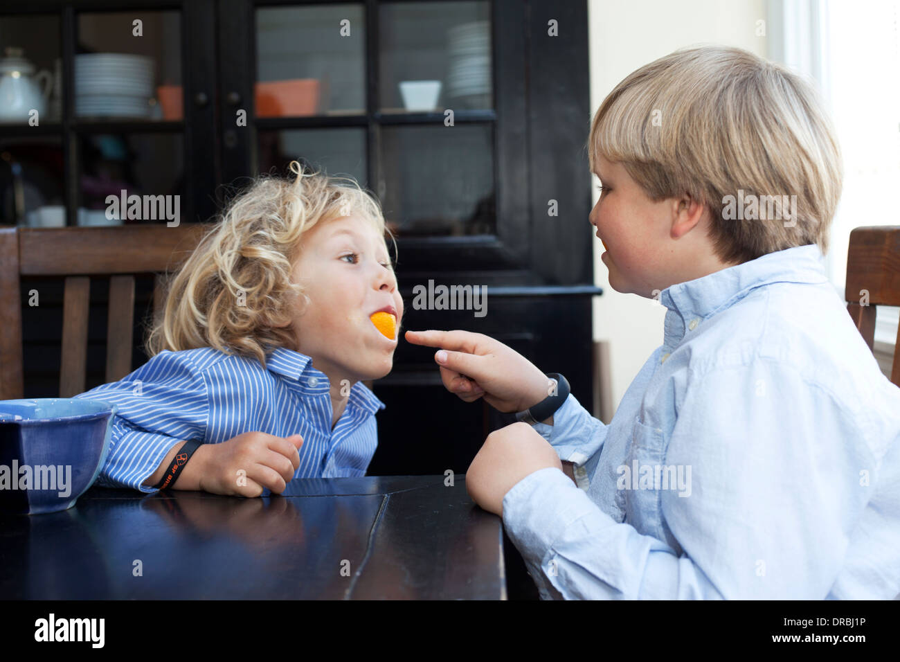 Fratelli giocando con la frutta di arancia al tavolo della cucina Foto Stock