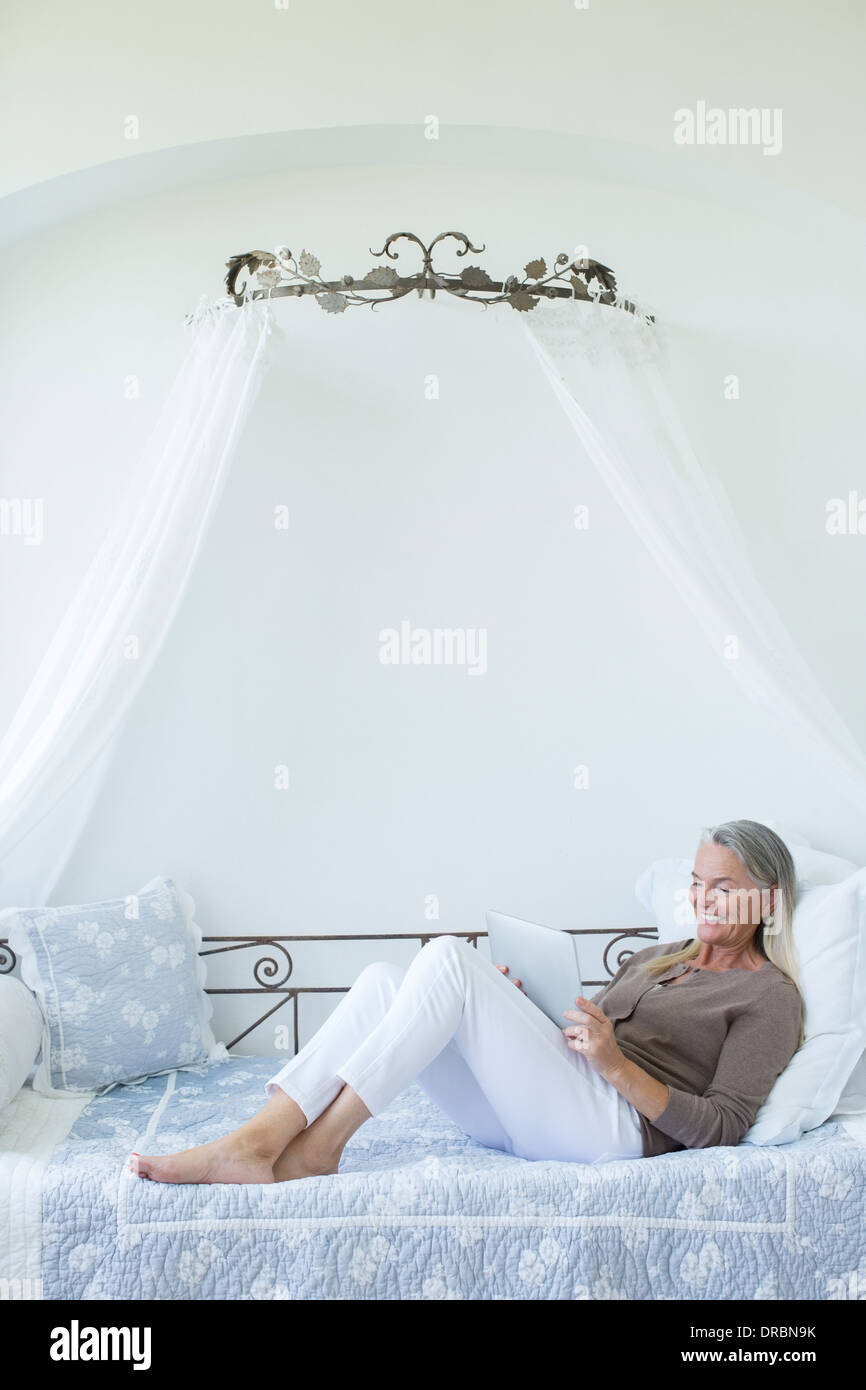 Senior donna con tavoletta digitale rilassante in divano letto Foto Stock