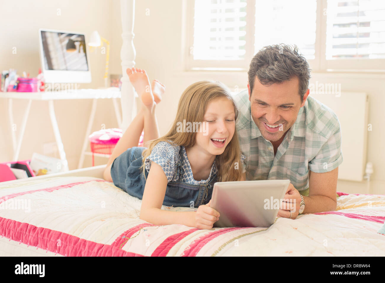 Padre e figlia con tavoletta digitale sul letto Foto Stock