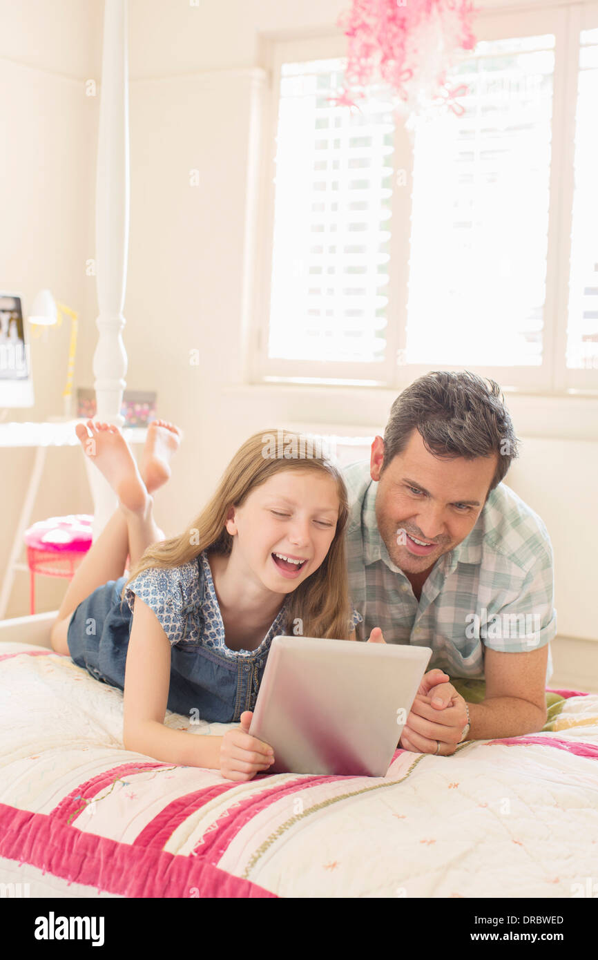 Padre e figlia con tavoletta digitale sul letto Foto Stock