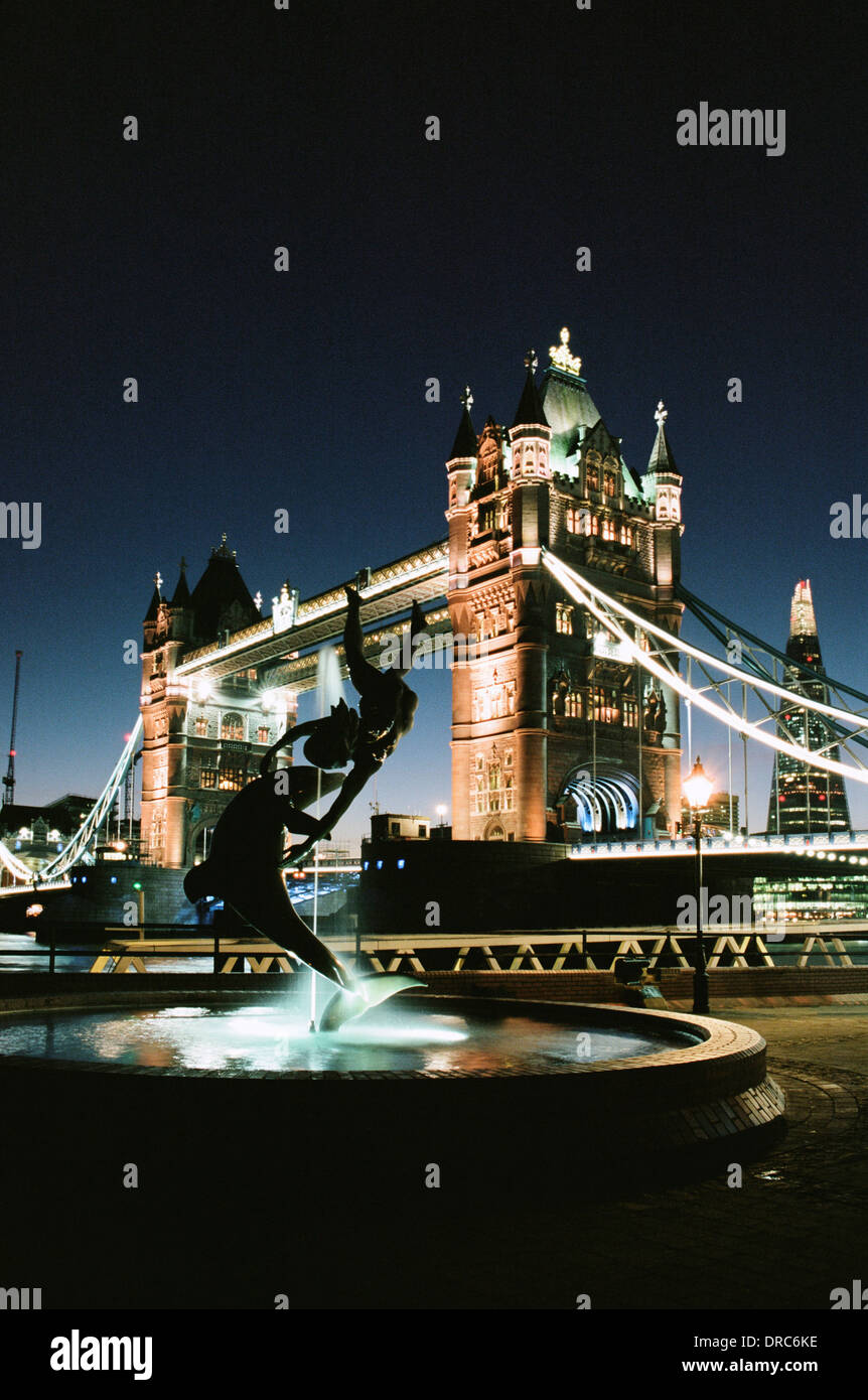 Il Tower Bridge di Londra, illuminata di notte, con la ragazza con la fontana dei Delfini e La Shard in background. Foto Stock