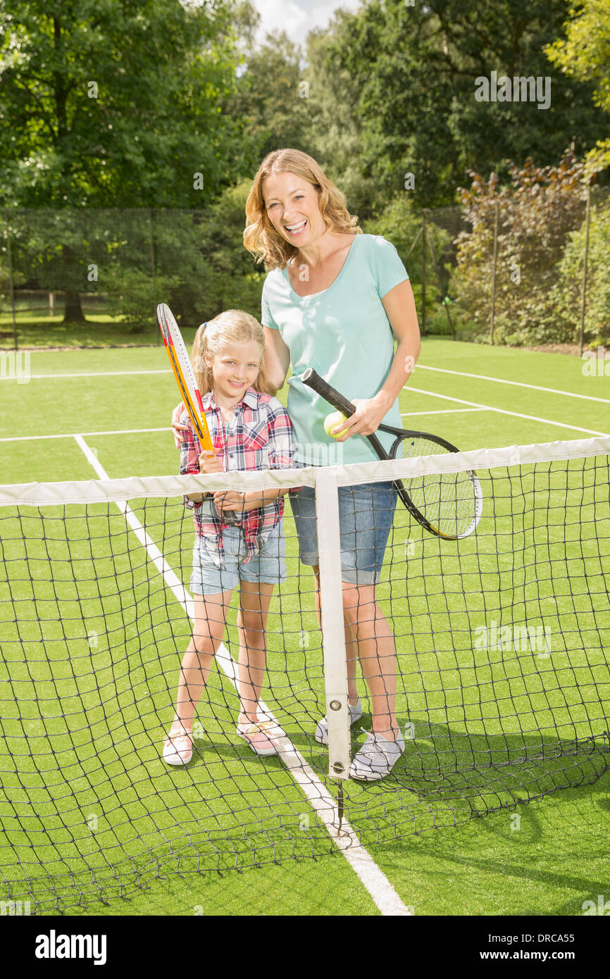 Madre e figlia sorridente sul campo da tennis d'erba Foto Stock