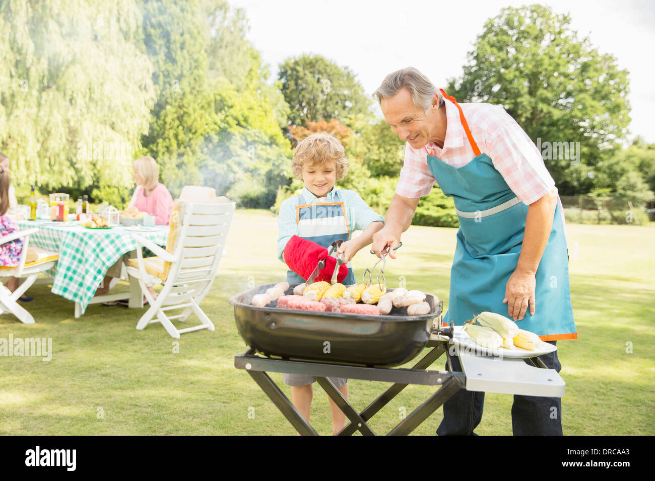 Nonno e nipote cuocere carne e mais su barbecue Foto Stock