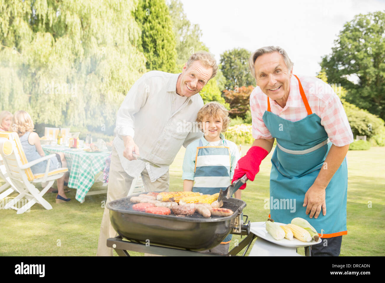 Multi-generazione uomini cuocere carne e mais a barbecue nel cortile posteriore Foto Stock