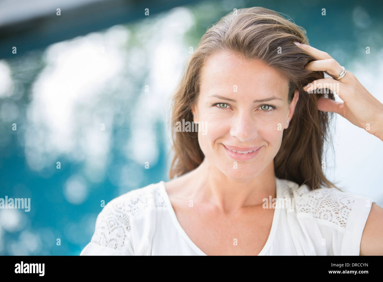 Donna sorridente con le mani nei capelli a bordo piscina Foto Stock