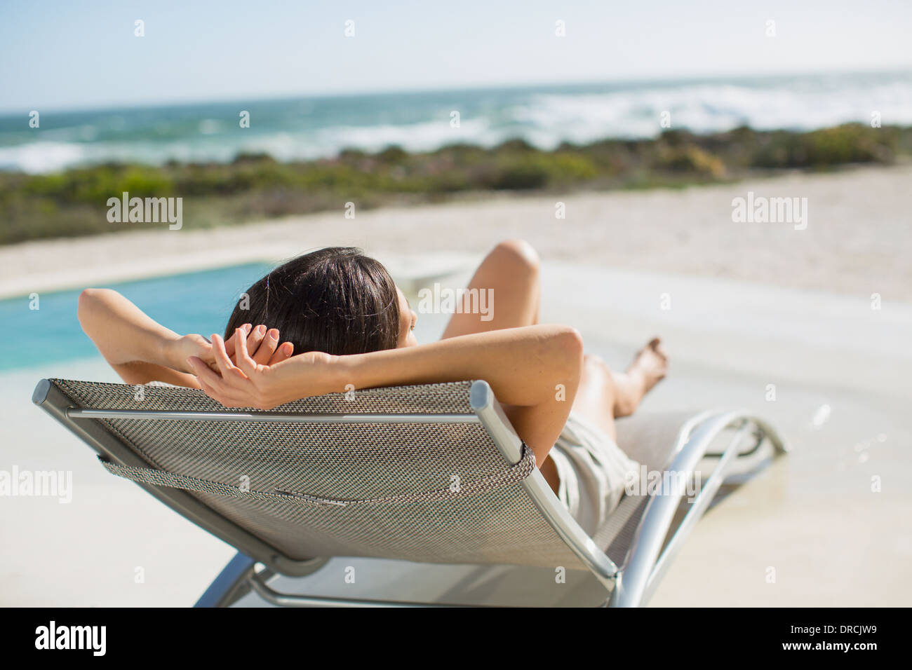 La donna a prendere il sole sulle sdraio a bordo piscina Foto Stock