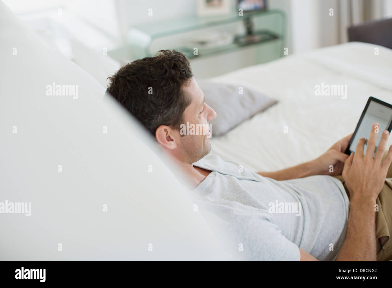 Uomo con tavoletta digitale sul letto Foto Stock