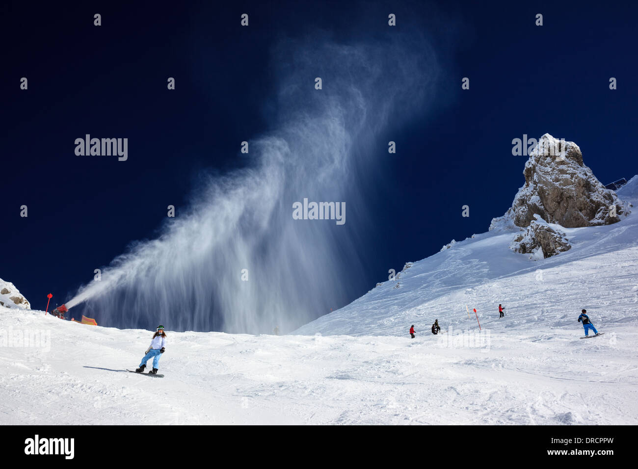 Snow making machine creando una nuvola di neve artificiale contro un profondo cielo blu nel villaggio austriaco di St Anton. Foto Stock