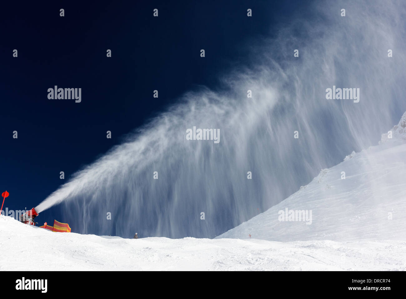 Snow making machine creando una nuvola di neve artificiale contro un profondo cielo blu nel villaggio austriaco di St Anton. Foto Stock